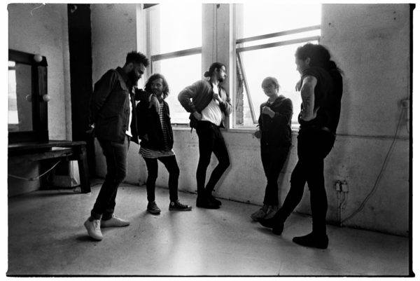The five members of Gang Of Youths stare out a window pensively, lost in thought.