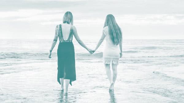 two women holding hands on beach